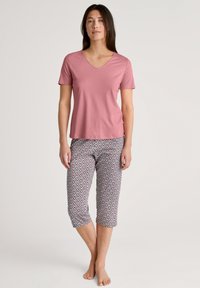 Roze v-hals t-shirt gecombineerd met capri-broek in een geometrisch patroon met rode en blauwe accenten. Zachte, lichte stof met een casual pasvorm.