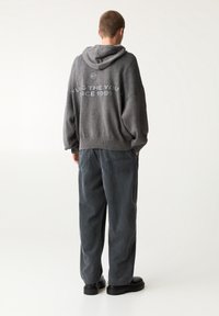 Szara, oversize bluza z kapturem o fakturowanym wykończeniu, z tekstem na plecach, w połączeniu z luźnymi, prążkowanymi spodniami z korduroy w ciemniejszym odcieniu szarości.