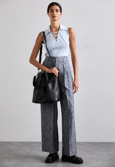 Top senza maniche di un blu chiaro con lacci davanti, abbinato a pantaloni larghi a quadri grigi e una borsa a secchiello nera in texture. Scarpe con plateau nere.