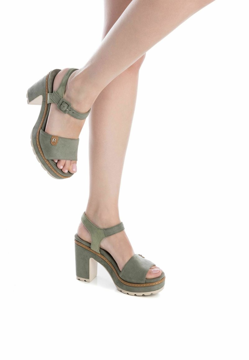 Sandali con tacco in suede verde, con cinturino alla caviglia, punta aperta e suola piatta bianca spessa. Logo del marchio ben visibile sul lato.