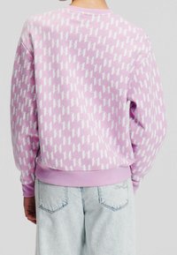 Lila sweatshirt med vitt geometriskt mönster, rund halsringning, långa ärmar och ribbad nederkant. Matchas med ljusblå denimjeans.