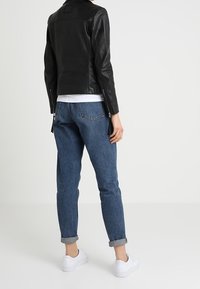 Black leather jacket with a fitted design, rolled sleeves, paired with mid-blue tapered jeans and white sneakers.