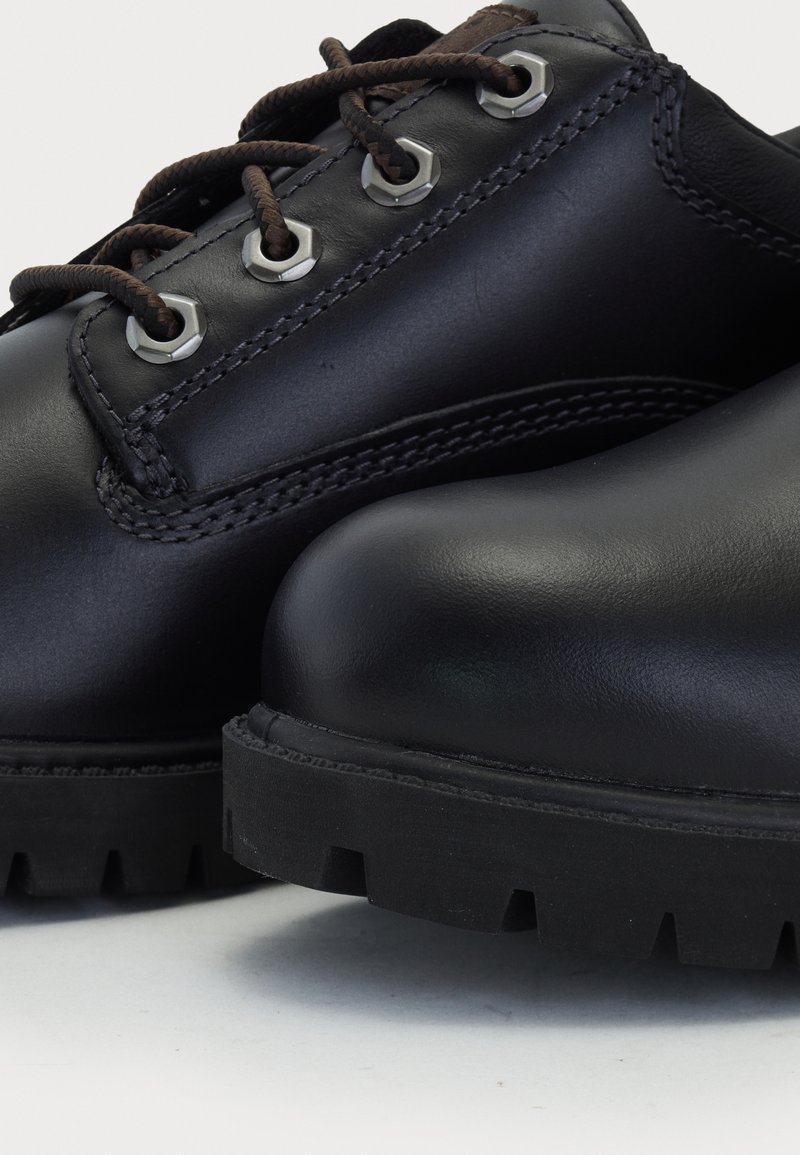 Black leather shoes with brown laces, round toe, silver eyelets, and a rugged black rubber sole featuring deep tread patterns.