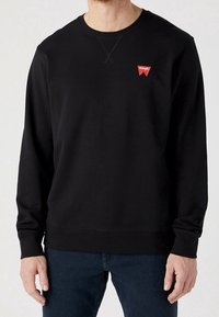 Svart långärmad sweatshirt i mjukt tyg, med rund halsringning, ribbade ärmslut och en liten röd logotyp på bröstet.