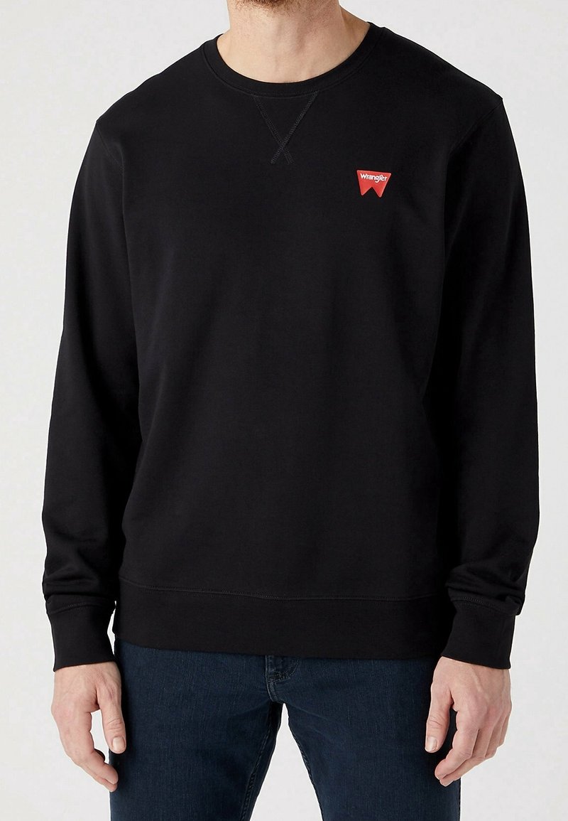 Svart långärmad sweatshirt i mjukt tyg, med rund halsringning, ribbade ärmslut och en liten röd logotyp på bröstet.