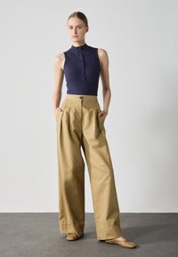 Top sin mangas de canalé en color azul marino con un alto cuello y cierre de botones, combinado con pantalones de pierna ancha en color beige que cuentan con bolsillos laterales y una cinturilla con botón.