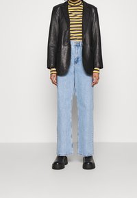 Svart läderblazer över en gul och svart randig polokrage, matchad med ljusblå vida jeans och svarta plattform stövlar.