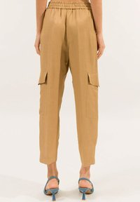 Pantaloni cargo color khaki con vita elastica, due tasche frontali e design a gamba affusolata. Texture liscia con una vestibilità casual.
