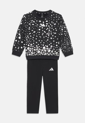 Juodas sportinis džemperis su sidabriniu leopardų raštu, apvalia iškirpte ir ribotu rankogaliais, derinamas su juodomis kelnėmis, ant kurių yra mažas baltas Adidas logotipas.
