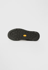 Sorte gummisåle med et teksturert mønster, som har dype spor og en metallisk Vibram-logo, designet for godt grep og holdbarhet.