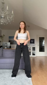 Jean noir à jambes larges avec une taille haute, comportant une fermeture à bouton et à glissière, associé à un top court blanc. Texture lisse.