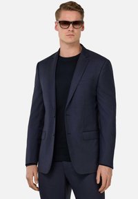 Navy blue suit jacket with a textured finish, two buttons, and notch lapels, worn over a black shirt. Features side pockets and tailored fit.