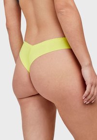Neon żółty thong o gładkiej fakturze, z falbaniastym pasem i minimalnym zasięgiem dla smukłego wzornictwa.