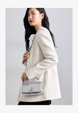 Borsa argento con una finitura testurizzata, caratterizzata da una tracolla a catena e un accento con logo, abbinata a un cappotto di lana crema.