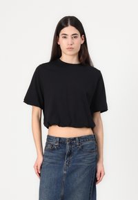 Fekete, pamutból készült, rövid ujjú cropped póló. A modell egy magas derekú farmer szoknyával párosítja, amely gombos záródással rendelkezik.