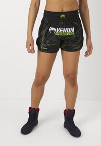 Black training shorts featuring green accents and a logo. Textured fabric with an elastic waistband, side pockets, and geometric lines.