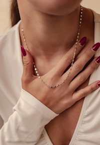 Collier en chaîne en argent avec des maillons allongés, porté autour du cou, avec une finition texturée et des accents réfléchissants étroitement espacés.