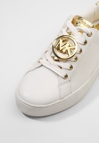 Sneaker bianco in pelle con logo in metallo dorato sulla linguetta, dettagli dorati all'interno, punta rotonda e laccio con occhielli in metallo.