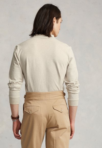 Light beige long-sleeve sweater with ribbed cuffs, paired with high-waisted, tan trousers featuring back pockets and adjustable side straps.