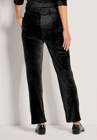 Zwarte fluwelen broek met een gladde textuur, voorzien van een relaxte pasvorm en elastische tailleband, gecombineerd met glanzende zwarte schoenen.