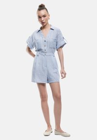 Blå- og hvidstribet kort jumpsuit med korte ærmer, knaplukning foran, to brystlommer og en tætsiddende talje. Bæres med lyse sko.