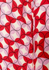 Rood en roze geometrisch stoffenpatroon met overlappende cirkels en vormen op een crème achtergrond. Bevat zwarte omlijningdetails.