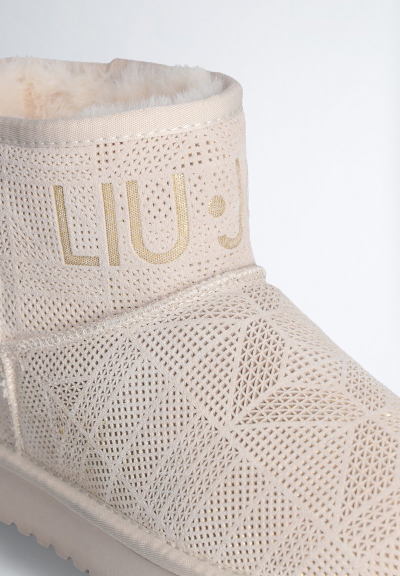 Hellbeige Knöchelschuh mit geometrischem Perforationsmuster, flauschigem Futter und goldener Schrift. Weiches Material mit strukturierter Oberfläche und Gummisohle.