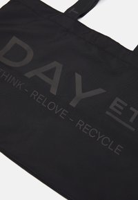 Czarna torba typu tote wykonana z tkaniny o fakturowanej powierzchni. Posiada wyraźne, tłoczone napisy: „DAY ET” oraz „THINK - RELOVE - RECYCLE”.
