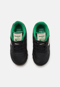 Zapatillas de cuero negro con acentos en verde y crema. Las características incluyen cierre con cordones, puntera perforada y suela de goma texturizada con agarre.