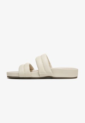 Light beige slide sandals featuring a broad double strap design, smooth leather texture, and a flat cushioned sole.