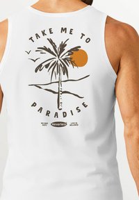 White sleeveless tank top featuring a brown palm tree graphic, orange sun, and text saying "TAKE ME TO PARADISE" with brand logo below.