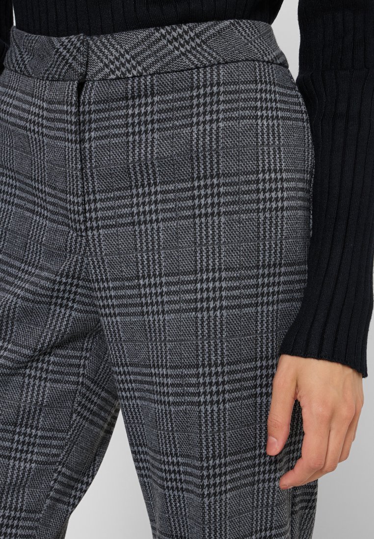Grau karierte Hosen mit hohem Bund, aus einem strukturierten Stoff und in taillierter Passform. Nahaufnahme, die das detaillierte Karomuster zeigt.