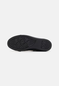 Schwarze Sneakersohle aus strukturiertem Gummi, mit geometrischen Profilmustern und einem glatten Kanten Design. Robuste und strapazierfähige Verarbeitung.