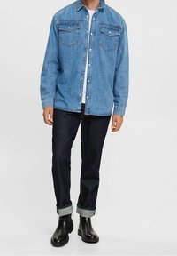 Riflová košile světle modré barvy s knoflíkovým zapínáním, dvěma předními kapsami a klasickým límcem, doplněn�á tmavými džíny a černými botami.