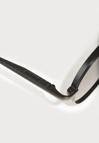 Ochelari de soare negri, cu un cadru metalic elegant și temporale din plastic texturat, având marca "FOSSIL". Vin cu lentile rotunde și detalii pe balamale.