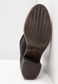 Bota de cuero negro con una suela de goma texturizada. La suela tiene un patrón trenzado y un ligero tacón. Talla 37 impresa en el costado.