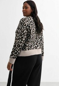 Leopardprint trui in beige en zwart, met ribbels aan de onderkant en mouwen. Draagt met zwarte broeken, wat een casual stijl toont.