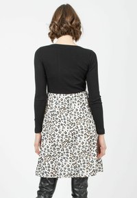Schwarzes geripptes Langarmoberteil kombiniert mit einem weißen Kleid mit einem schwarz-braunen Leopardenmuster, getragen mit schwarzen Lederhosen.