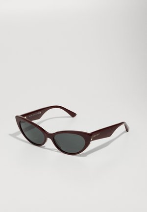 Lunettes de soleil œil de chat bourgogne avec des verres foncés, monture en plastique lisse et accents dorés sur les côtés. Design stylé et angulaire.