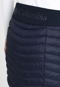 Marinblå vadderad kjol med ett kviltat mönster. Har en elastisk midja med "Columbia"-logotyp. Materialet är lätt och slätt.