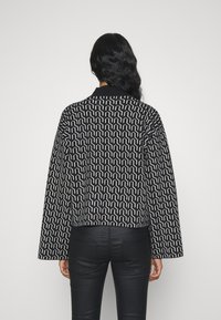 Black and white patterned jacket with wide sleeves, featuring geometric design. Solid black collar and back, paired with fitted black pants.