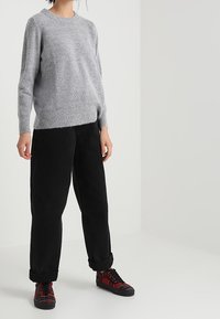 Gray, fluffy knit sweater with a round neckline, paired with black, loose-fit trousers and red plaid sneakers. Relaxed outfit suitable for casual wear.