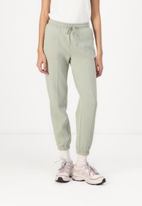 Lichtgroene joggingsbroek van zacht materiaal, met een elastische tailleband met trekkoord, boorden bij de enkels en zijnaaddetails.