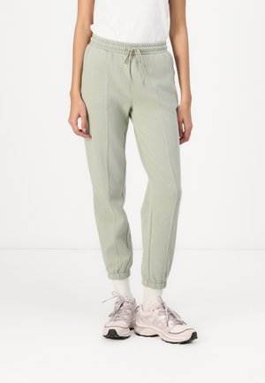 Lys grønne joggebukser laget av myk stoff, med elastisk linning og snor, mansjetter ved anklene og detaljer i sidesømmen.