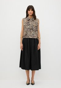 Mouwloze top met luipaardprint en kraag, gecombineerd met een zwarte, lange rok. Accessoires zijn onder andere gouden armbanden en zwarte hakschoenen.