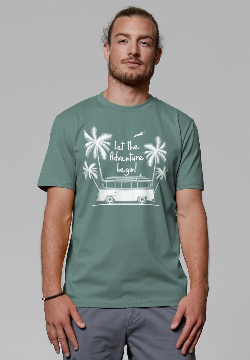 Groene t-shirt met witte grafiek van een bus met palmbomen en de tekst "Laat het avontuur beginnen!" Zacht materiaal, ronde hals ontwerp.