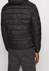 Czarna kurtka puchowa z poziomym pikowaniem, kapturem i elastycznymi mankietami. Materiał jest błyszczący i lekki, zapewniając izolację.