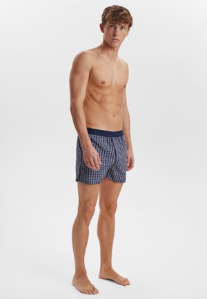 Boxer in cotone con motivo a quadretti blu navy, vita elastica e vestibilità ampia. Il tessuto presenta una texture sottile.