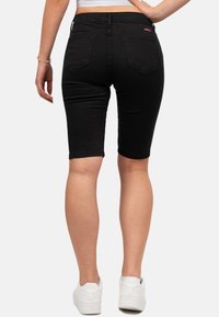 Bermudas en denim noir avec une coupe ajustée, des poches arrière et un ourlet retroussé, assorties à des baskets blanches.