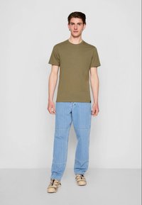 T-shirt de algodão verde-oliva combinada com jeans de denim listrados em azul claro. Corte casual, mangas curtas e decote redondo. Sapatos bege completam o visual.